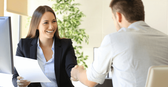 A woman in an office holding a piece of paper shaking another person's hand