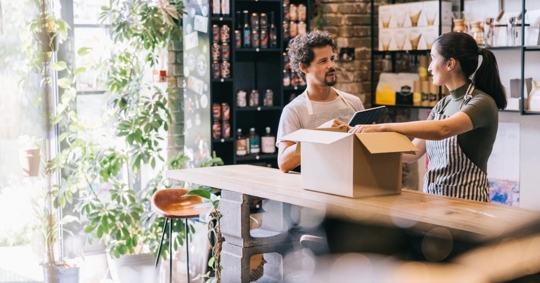 Standing at the counter, the female owner engages in a lively discussion with her colleague while preparing an online order