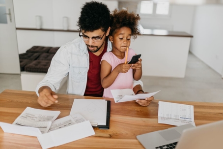 Father doing finances with his young daughter sitting in his lap.